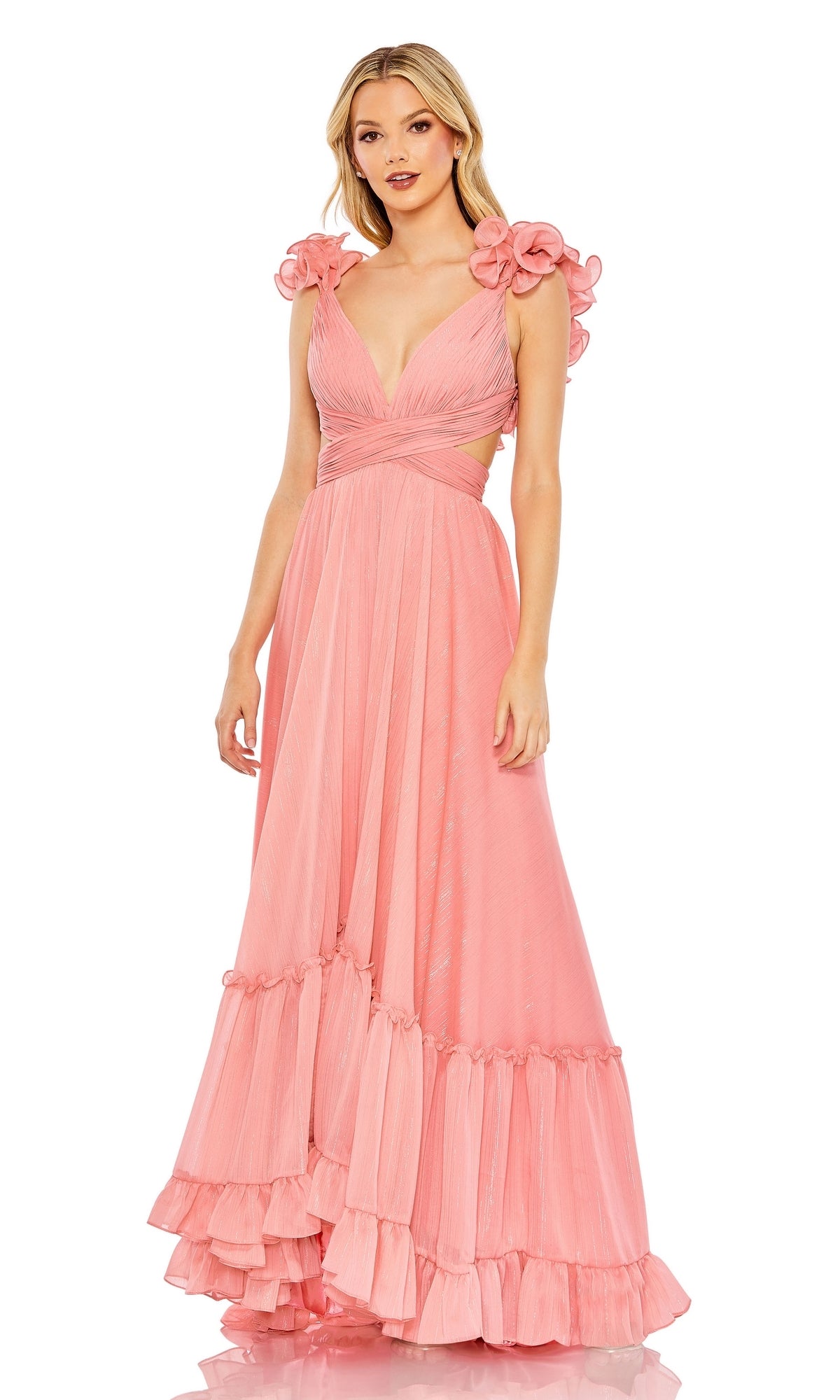 A woman in the Mac Duggal 68094 Lace-Up Ruffled Formal Gown, a sleeveless floor-length pink dress with ruffle details and floral shoulder accents, stands facing forward.